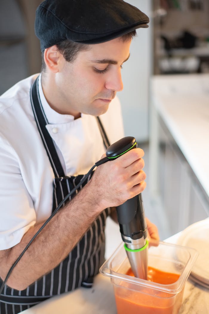 Chef blending soup with immersion blender, showcasing culinary skills in a modern kitchen.